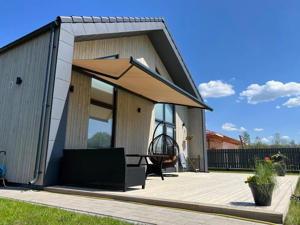 Motoriserad beige terrassmarkis utfälld på modern trähusfasad med terrass